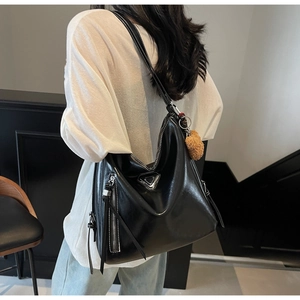 Detail of black glossy leather bucket bag with metal logo and cute plush bear charm