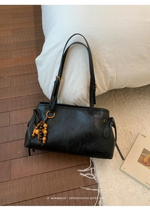 Minimalist black leather tote bag featuring a retro wooden bead tassel on a wooden floor