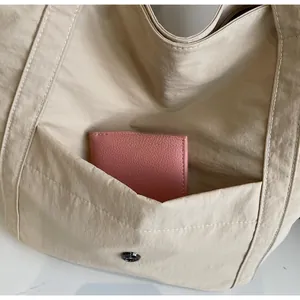 Close-up of beige nylon tote bag showing front pocket with magnetic buckle and wallet