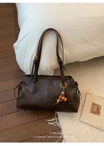 Detail of retro dark brown tote bag with wooden bead charm in a minimalist interior setting