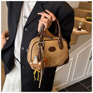 Detail view of khaki patchwork pillow bag with plush bear charm and brown handles