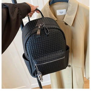 Detail of black woven leather backpack with silver bear charm held by a model
