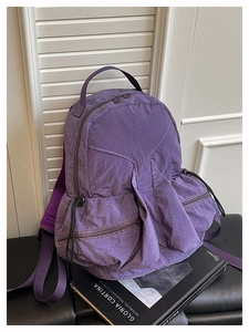 Detail of purple wrinkled fabric backpack with multiple zipper pockets on leather seat