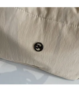 Detail of beige canvas tote bag showing the round black metal logo and textured fabric