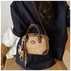 Brown vintage style satchel bag with plush bear charm worn by model in black suit