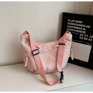 Detail of pink quilted dumpling bag featuring blue butterfly embroidery and wide strap