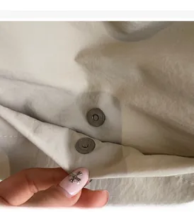Detail of light beige fabric lining with two dark grey magnetic metal buckles on tote bag