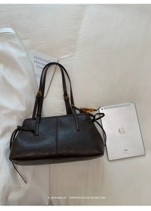 Detail of dark brown leather tote with bow accents and wooden bead pendant on white fabric