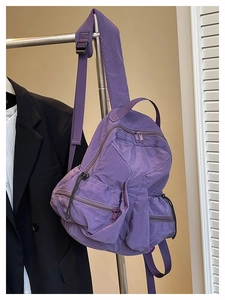 Detail of purple plaid nylon backpack featuring multiple functional zipper pockets and straps