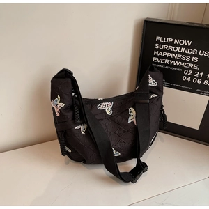Detailed view of black quilted crescent bag with colorful butterfly embroidery and wide strap