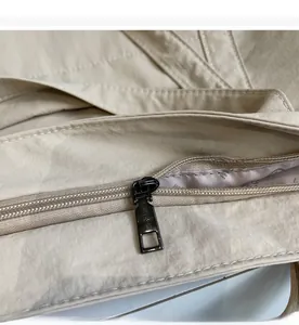 Detail of a smooth metal zipper and light grey letter-printed lining on a beige tote bag