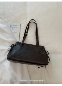 Detail of dark brown leather tote bag with gold buckle and drawstring side accents