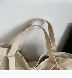 Close-up of reinforced double stitching on the handle of a beige nylon tote bag
