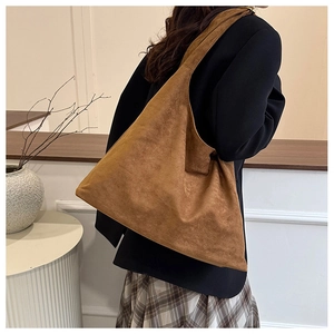 Grand sac à bandoulière en daim marron porté par un mannequin dans une pièce épurée