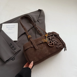 Close-up of dark brown suede shoulder bag with gold buckles and creative metal charms