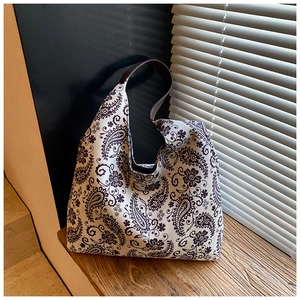 Detailed view of the paisley canvas tote bag with premium brown leather straps on wood surface