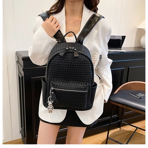Detail of black woven leather backpack showing silver zippers and cute bear charm