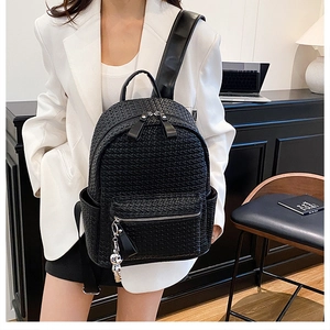 Detail of black woven leather backpack showing metal bear charm and side pocket texture