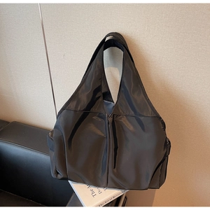 Détail d'un cabas noir en nylon avec de larges anses posé contre un mur texturé