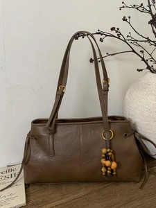 Vintage brown leather tote bag with wooden bead charm on a rustic wood surface