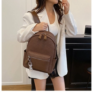 Detailed side view of brown woven leather backpack with silver bear charm and pocket
