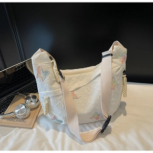 White crescent canvas bag with butterfly embroidery next to a laptop and headphones