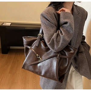 Detail of dark brown tote bag featuring glossy texture and decorative buckle straps