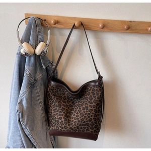Detail view of leopard print tote bag with brown leather handles on wooden hook