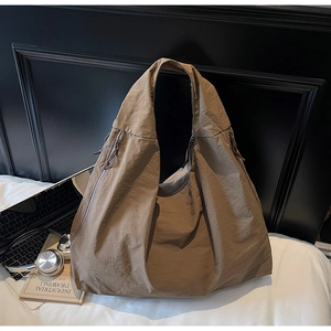 Vue détaillée du sac hobo en nylon marron avec fermetures éclair sur lit blanc élégant
