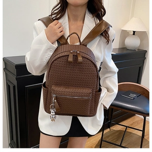 Detail of dark brown woven leather backpack worn by model showing texture and bear charm