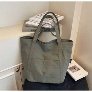 Detail of sage green canvas tote bag with front pocket and round metal logo on cabinet