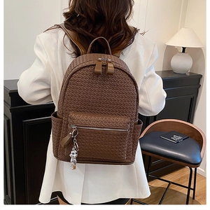 Detail of dark brown woven texture backpack with silver zipper and bear pendant