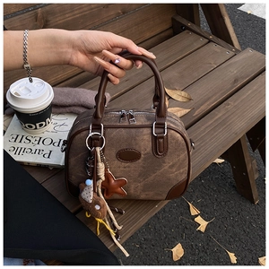 Detailed view of dark brown vintage Boston bag with plush bear charm on a wooden bench