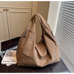 Détail du sac hobo en nylon marron clair avec zip latéral à côté d'un ordinateur