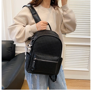 Detailed view of black woven faux leather backpack with metallic bear charm and zip pocket