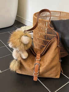 Brown woven bucket bag with lion pendant on a textured tile background