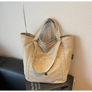 Detail of beige nylon tote bag featuring front pocket and woven label beside a book