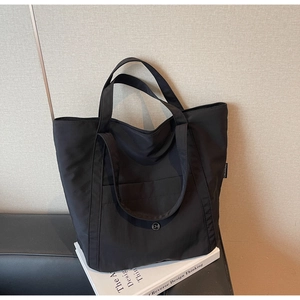 Detail of a black nylon tote bag featuring a round metal buckle and woven side label