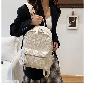 Detail of cream woven leather backpack with cute metal bear pendant on a black blazer