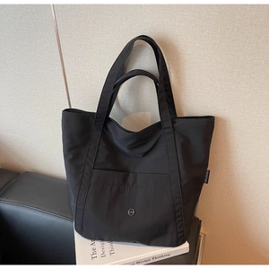 Detail view of black nylon tote bag with metal CM logo and spacious front pocket