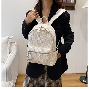 Detail of white woven texture backpack featuring a silver bear pendant and leather straps