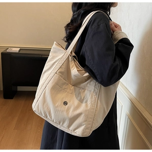Detail of a large beige nylon tote bag featuring a front pocket and round metal logo