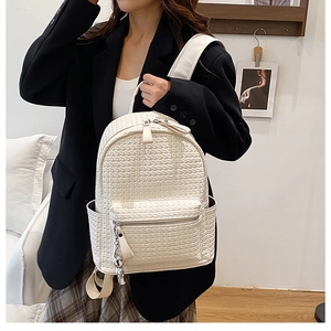 Close-up of white woven texture backpack with silver bear charm on zipper detail
