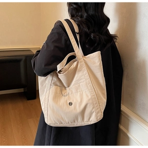 Detail of a large beige canvas tote bag with a front pocket shown on a model's shoulder
