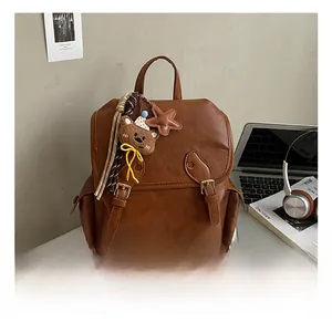 Detail of dark brown vintage faux leather backpack with metallic buckle and plush bear charm