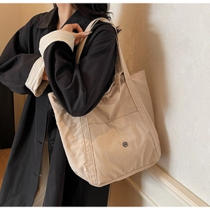 Beige oversized tote bag detail with metal logo and pleated texture on model shoulder