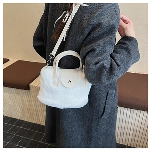 Close-up of a white plush crossbody bucket bag with silver buckle on a grey coat