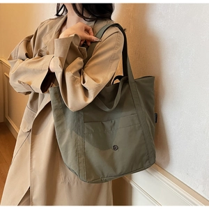 Detailed close-up of large olive green canvas tote bag with front snap pocket on a shoulder