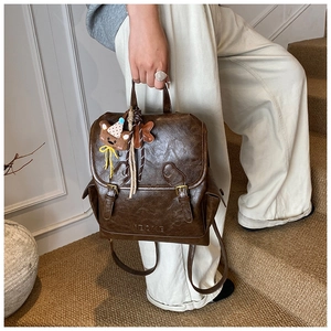 Detail of dark brown vintage faux leather backpack with decorative buckle and bear charm