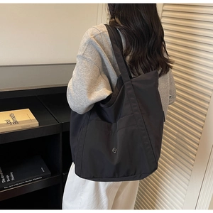 Detail showing the black nylon tote bag worn on shoulder with silver metal logo
